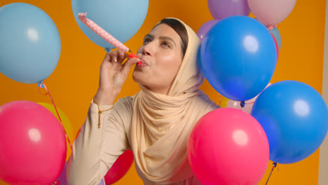 Studioporträt-Einer-Frau-Mit-Hijab,-Die-Geburtstag-Mit-Luftballons-Und-Partygebläse-Feiert